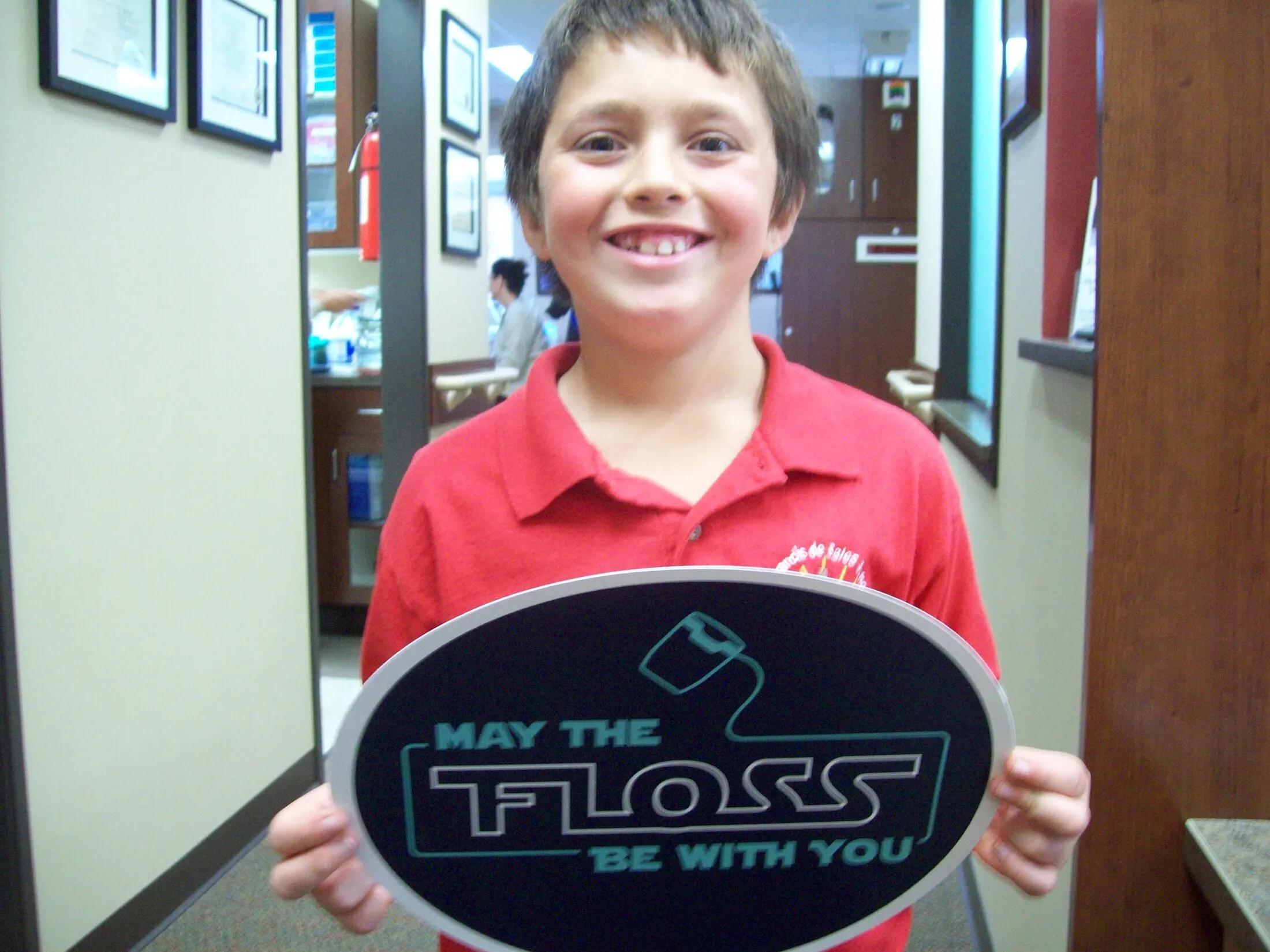 Young patient holding a “May the Floss Be With You” sign in the office.